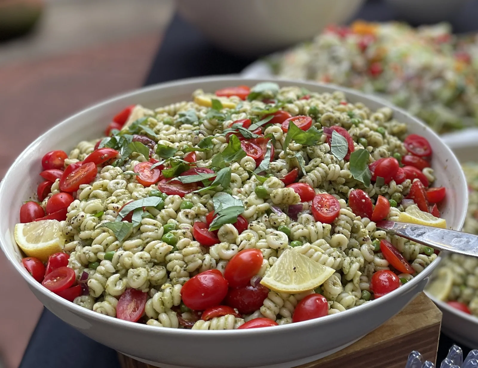 A bowl of pesto rotini salad with cherry tomatoes, peas, basil and lemon