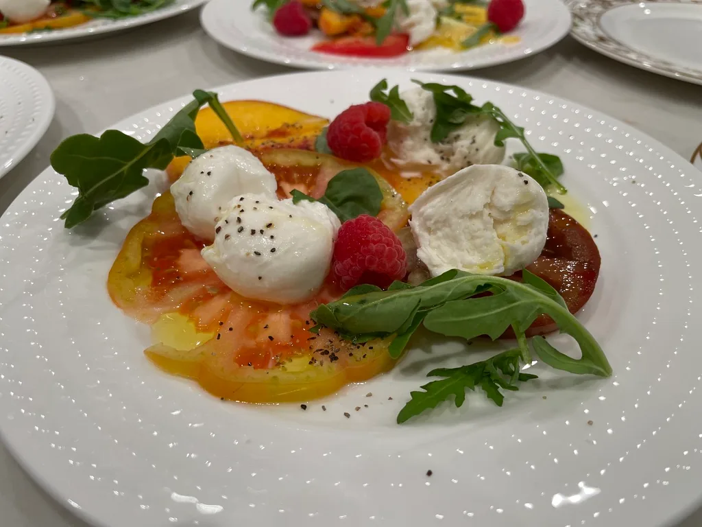 Burrata with heirloom tomato, strawberries, raspberries and arugula on a white plate