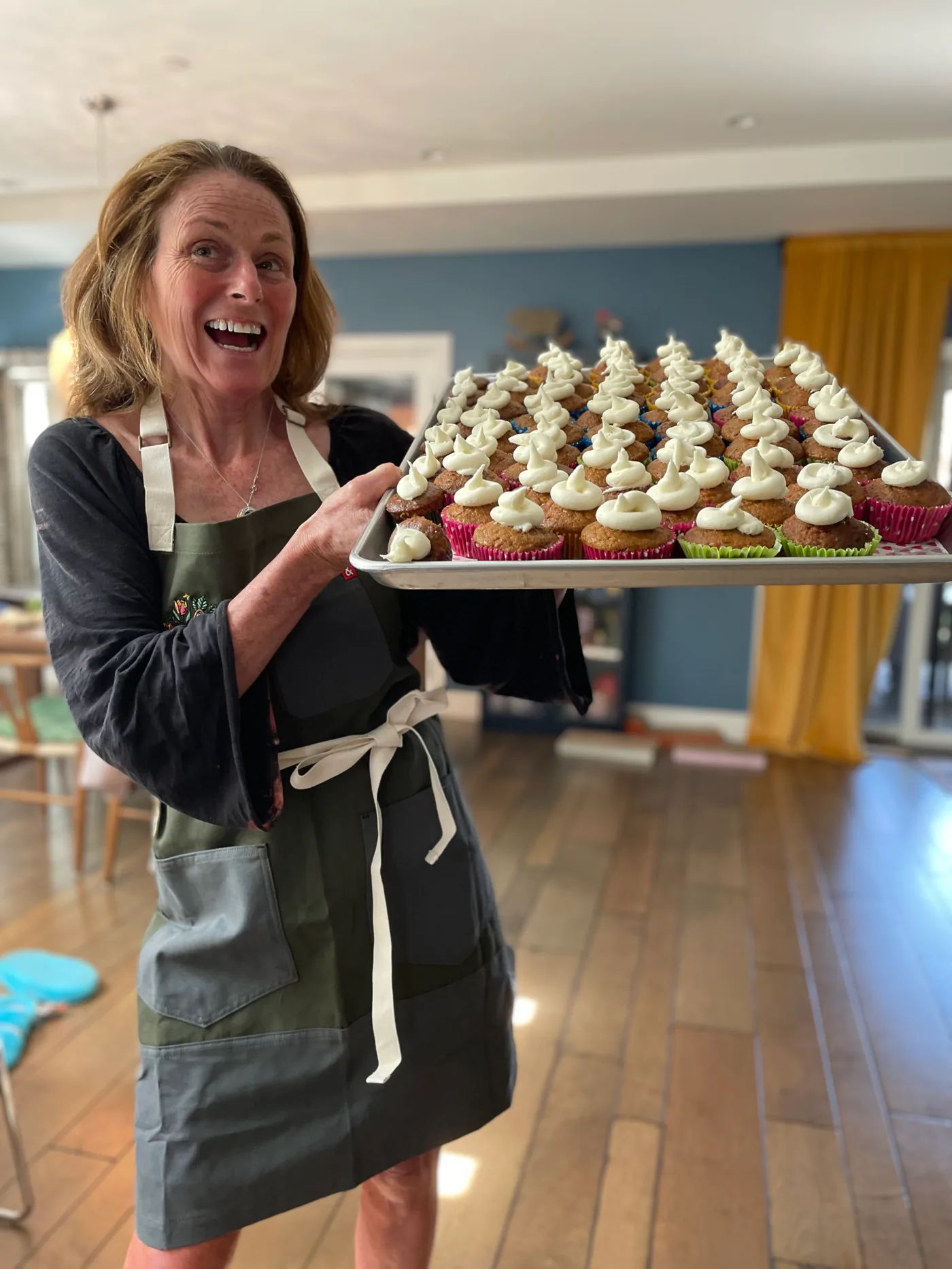 Chef Mylène laughing as she holds up a tray of frosted mini cupcakes
