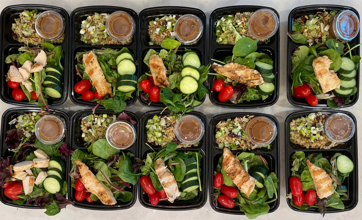 Rows of individual meal boxes with grilled chicken, cucumber, tomatoes, greens and dressing cups
