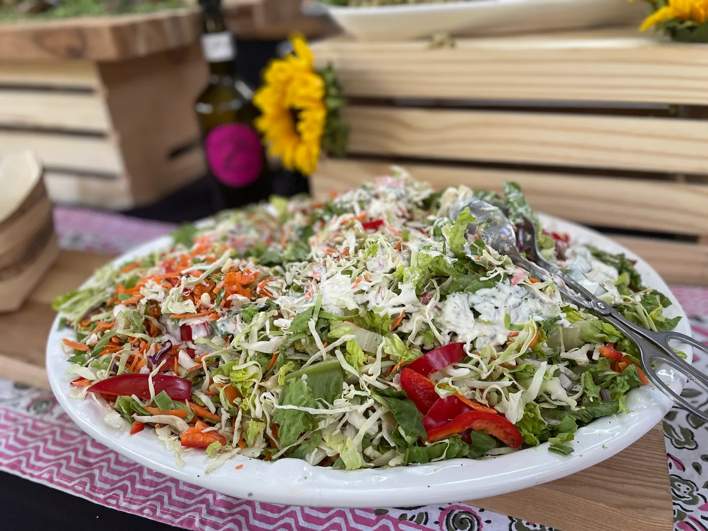 A large platter of shredded salad with peppers and herbs, served with tongs